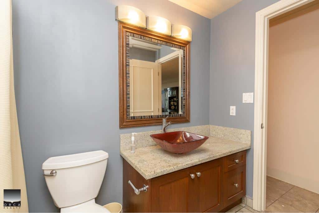 Modern bathroom with blue walls, wooden vanity, granite countertop, stylish red vessel sink, large mirror, and contemporary lighting, perfect for a Vancouver Island home.