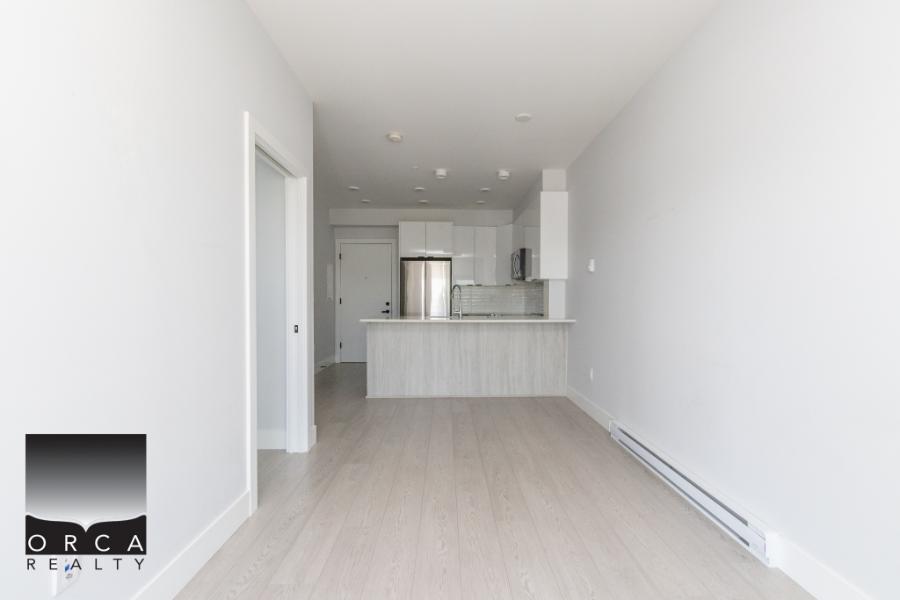 Modern open-concept kitchen and living area in a contemporary Vancouver home, showcasing bright white walls, stainless steel appliances, and minimalist design, ideal for buyers seeking stylish real estate.