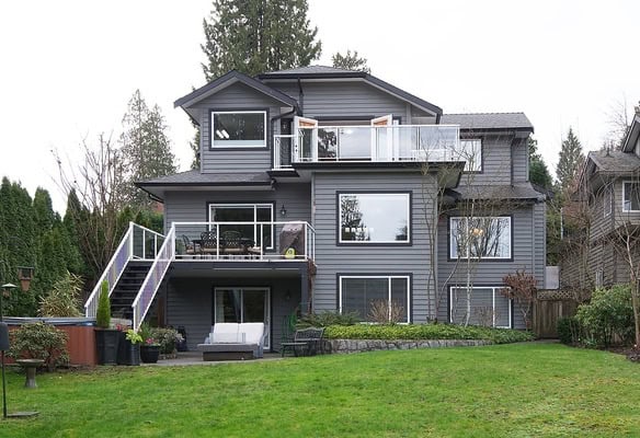 Spacious modern grey house with multiple balconies and large windows, surrounded by lush greenery and a well-maintained lawn, showcasing prime real estate in Vancouver.