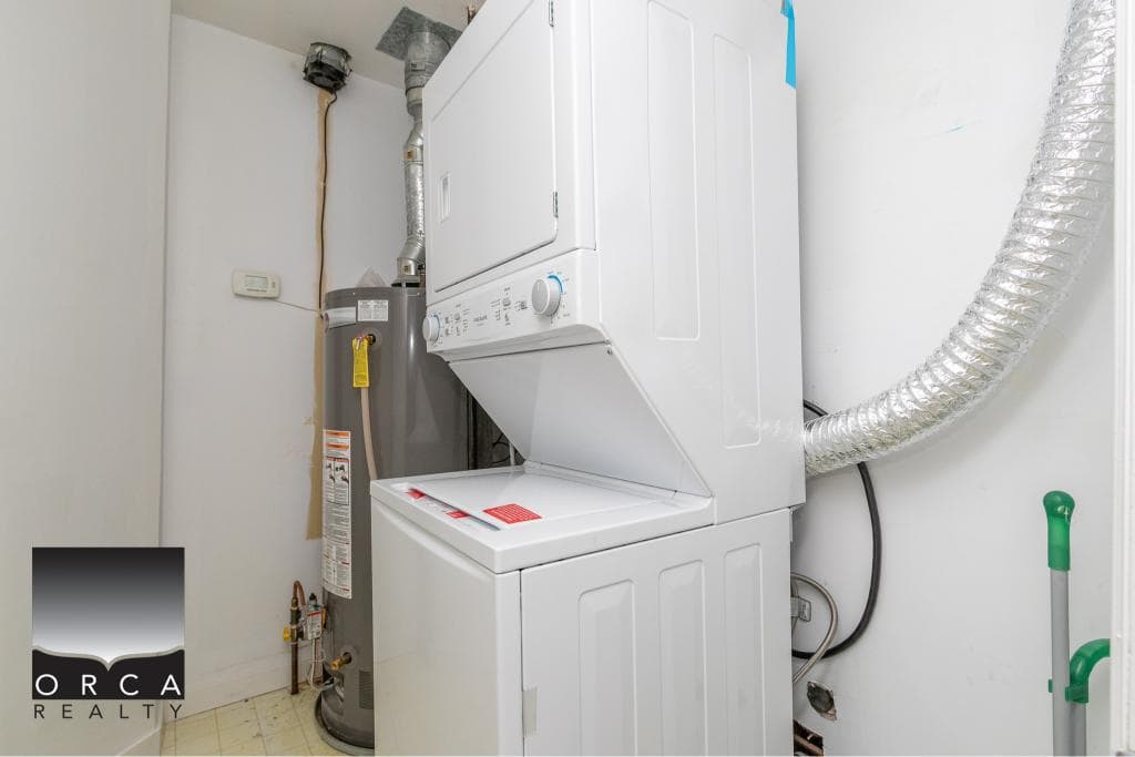 New laundry area with stacked washer and dryer units, water heater, and ventilation duct in a residential home - Orca Realty Inc.
