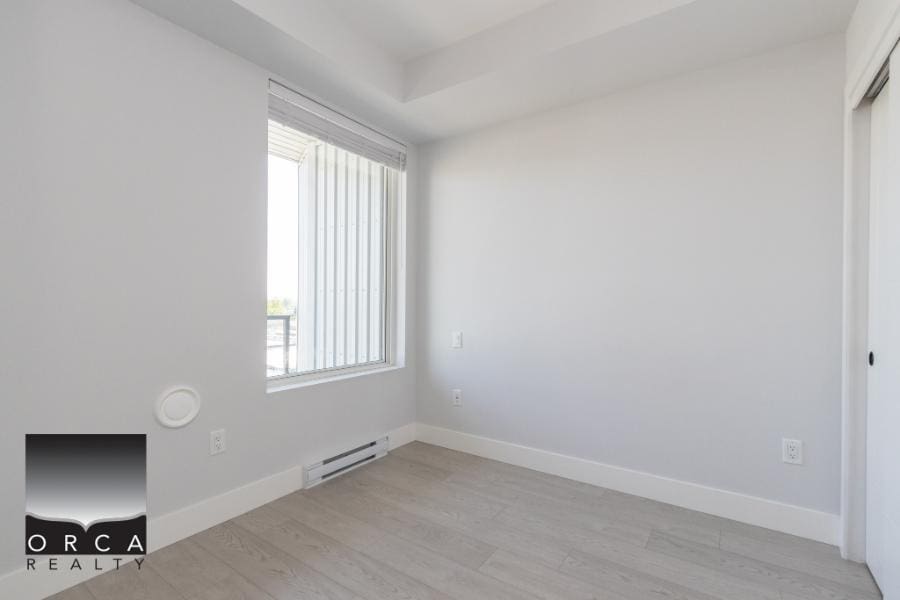 Bright empty bedroom with large window, white walls, light wood flooring, and modern minimalist design, perfect for real estate listing or property showcase in Kelowna or British Columbia.