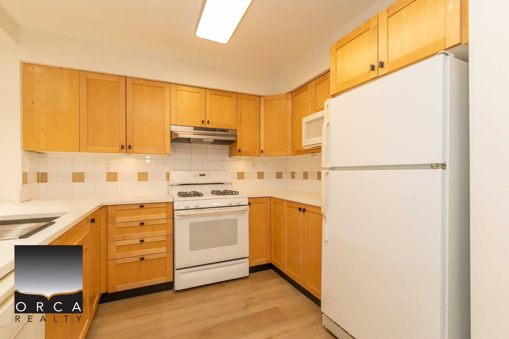 Bright kitchen with wooden cabinets, white appliances, and beige tile backsplash, ideal for cooking and entertaining in a cozy home.