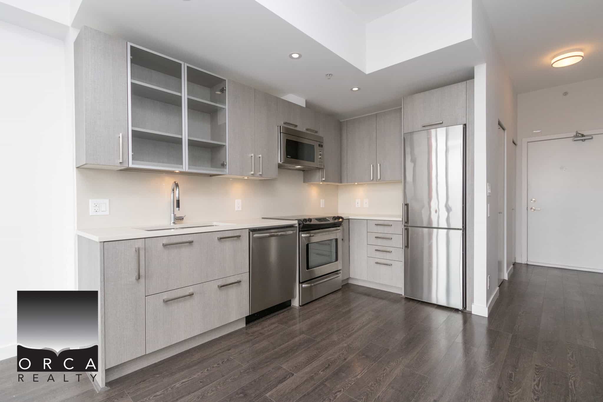 Modern grey kitchen with stainless steel appliances, minimalist cabinetry, and dark hardwood flooring, showcasing a stylish and functional space ideal for urban living.
