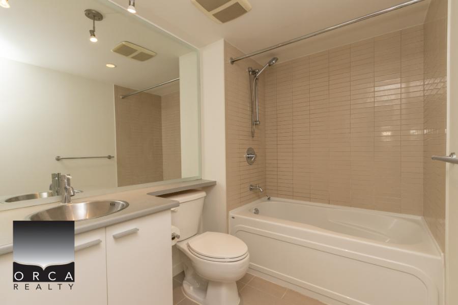 Modern bathroom with bathtub, shower, white fixtures, and beige tile wall - ideal Ottawa real estate bath for sale or rent.