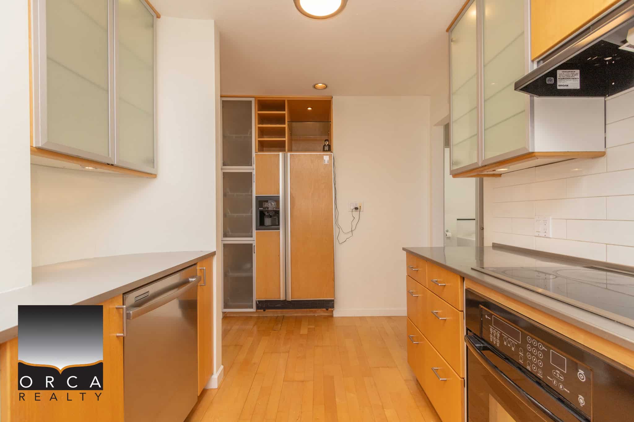 Modern kitchen with wooden cabinets, stainless steel appliances, and hardwood flooring, showcasing a functional layout perfect for Vancouver real estate listings.