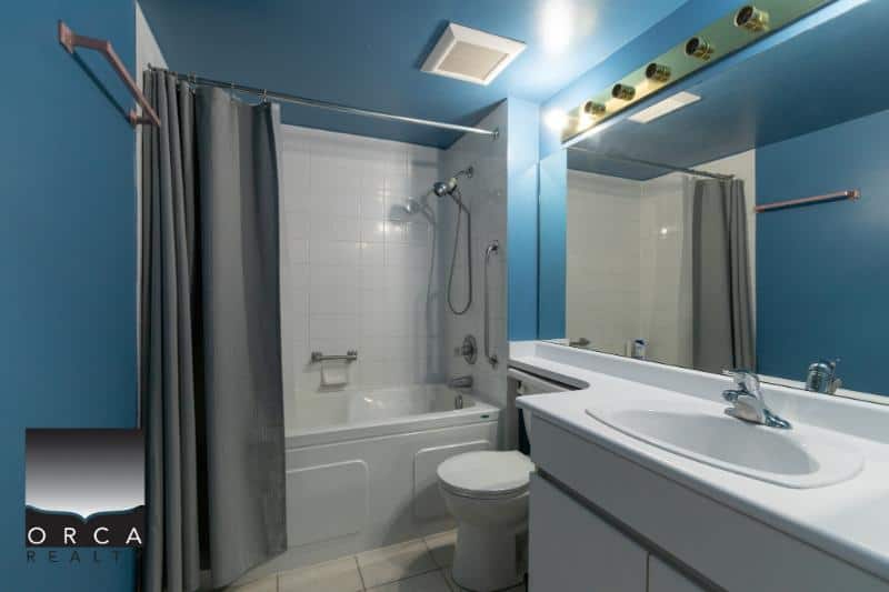 Bright blue bathroom with bathtub, shower, and vanity featuring a large mirror, modern fixtures, and grey towels; ideal for showcasing property features.