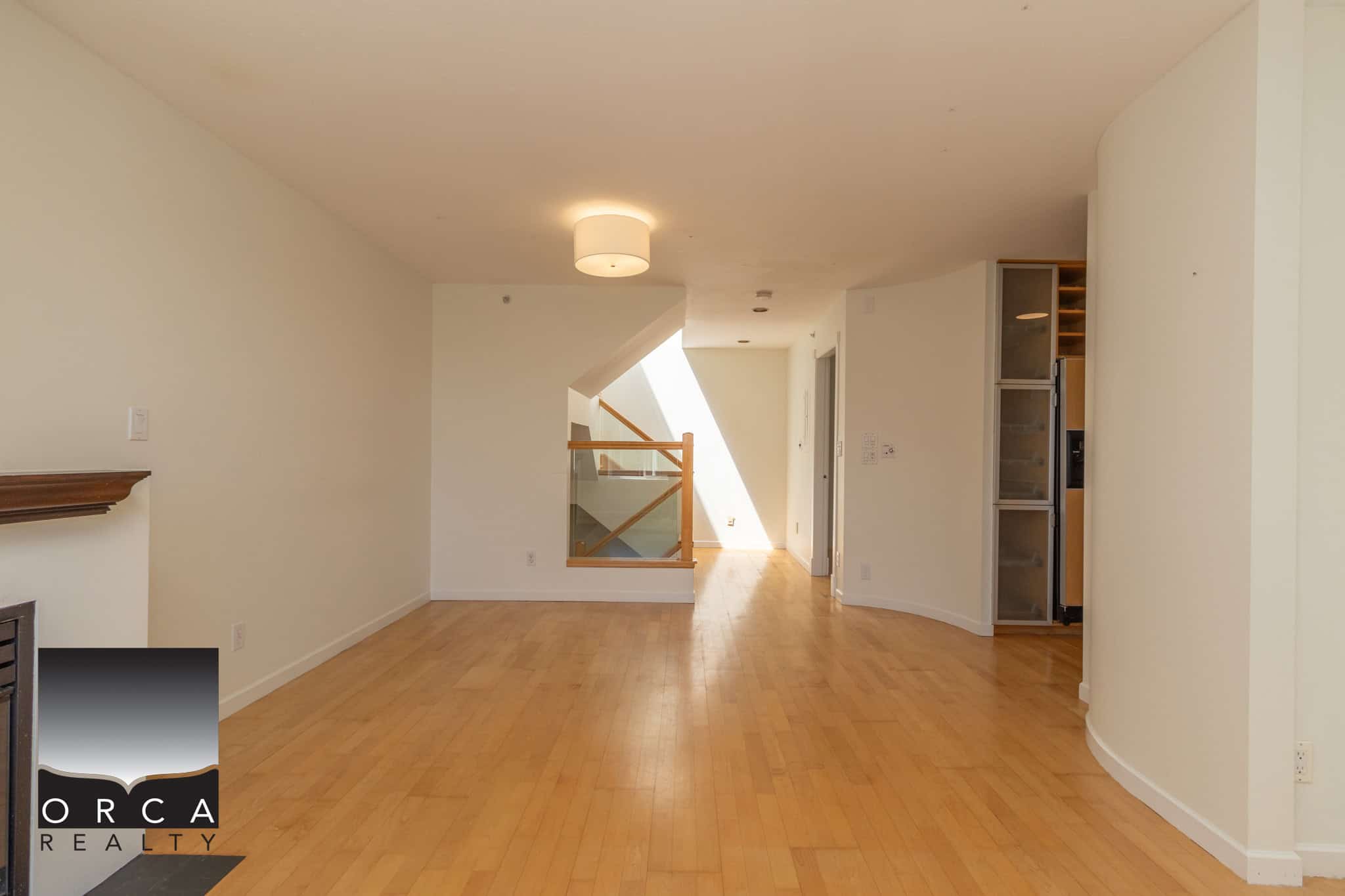 Spacious empty living room with hardwood floors and modern lighting, part of a residential property listed by Orca Realty Inc., ideal for homebuyers and real estate enthusiasts in Canada.