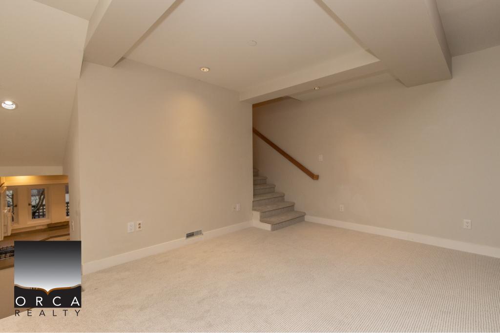 Bright and spacious home interior with neutral wall colours and plush carpet, featuring a staircase with a wooden handrail, perfect for family living and showcasing Orca Realty's premier property listings.