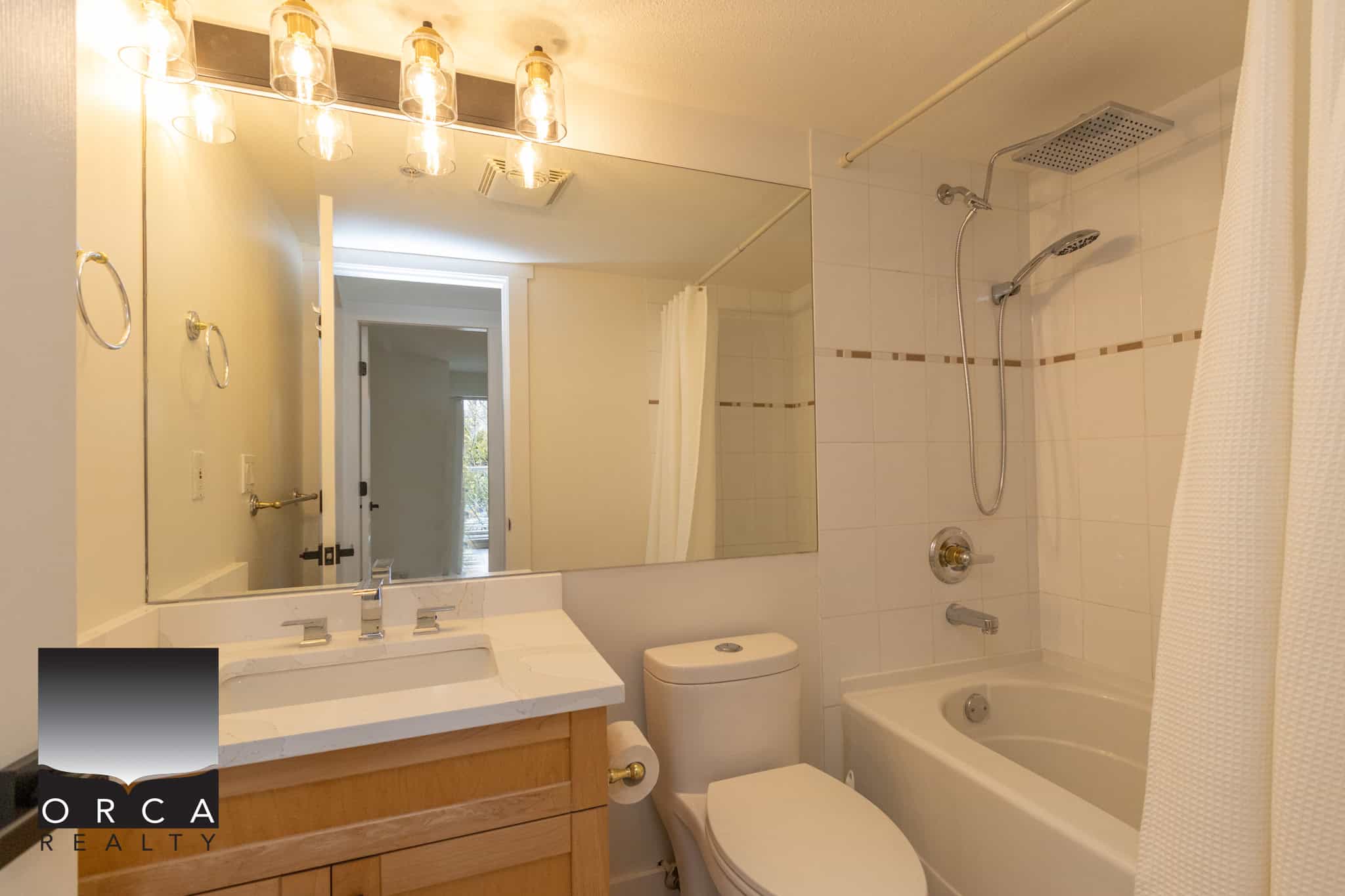 Bright modern bathroom with white tiles, bathtub, and showerhead, featuring a large mirror, vanity with sink, and natural light, ideal for Vancouver Island real estate listings.
