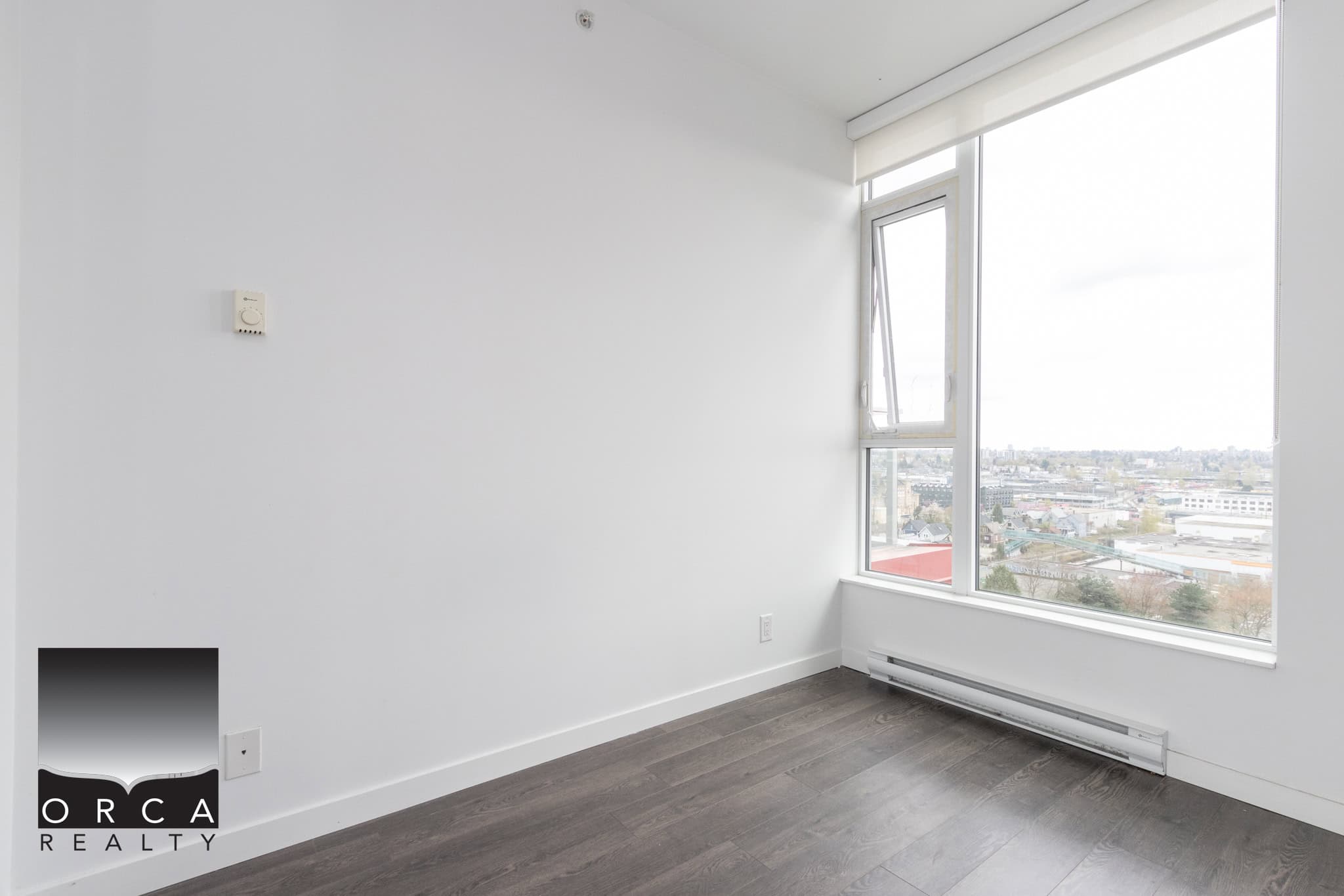 Modern empty city-view apartment room with large windows, white walls, and dark hardwood flooring, ideal for urban living and real estate investment in Vancouver, BC.