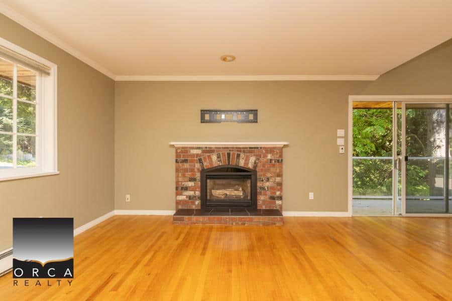 Cozy living room with brick fireplace and hardwood flooring, ideal for family gatherings and relaxation, featuring large windows and a sliding door to a backyard patio.
