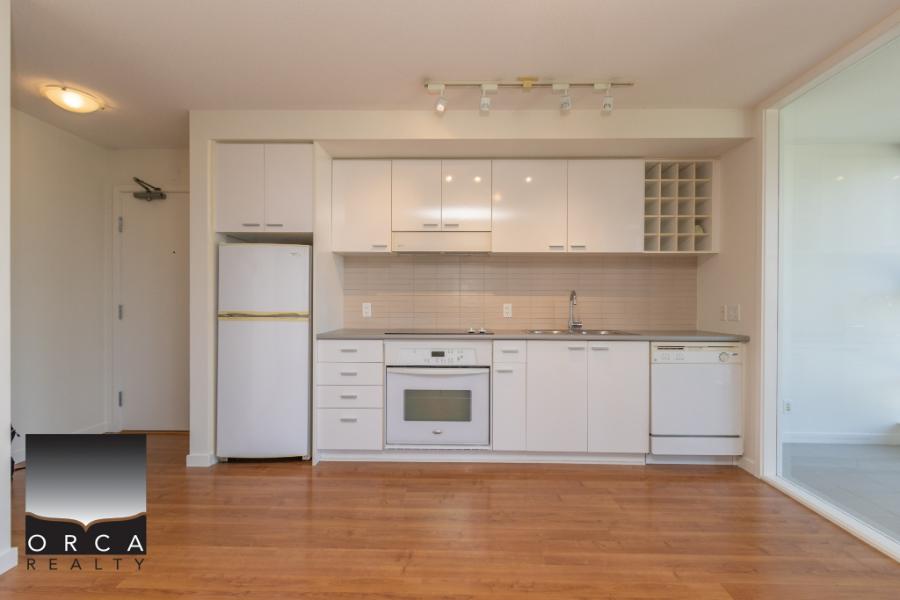 Modern white kitchen with built-in oven, refrigerator, dishwasher, and ample cabinet storage in a contemporary condo by Orca Realty Inc.
