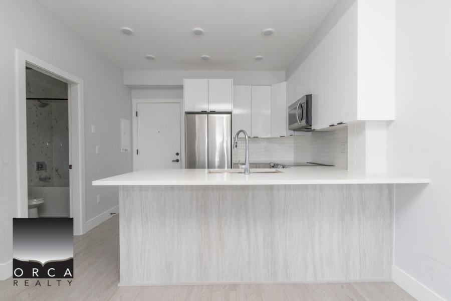 Modern kitchen with sleek white cabinetry, stainless steel appliances, and a spacious island, perfect for Vancouver area living and real estate investments.