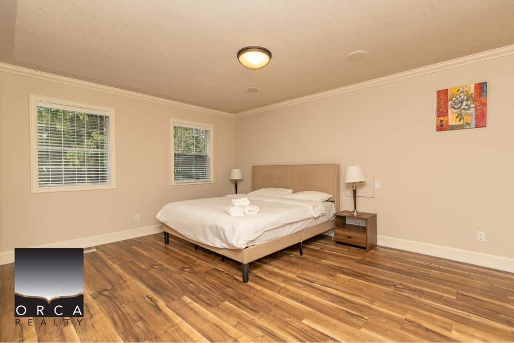 Spacious modern bedroom with large windows, minimalistic decor, and hardwood flooring, ideal for Vancouver Island real estate buyers seeking comfortable and stylish home interiors.