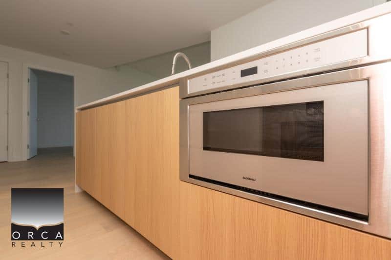 Modern kitchen with built-in stainless steel microwave and light wood cabinetry, ideal for Vancouver real estate listings and home staging by Orca Realty Inc.