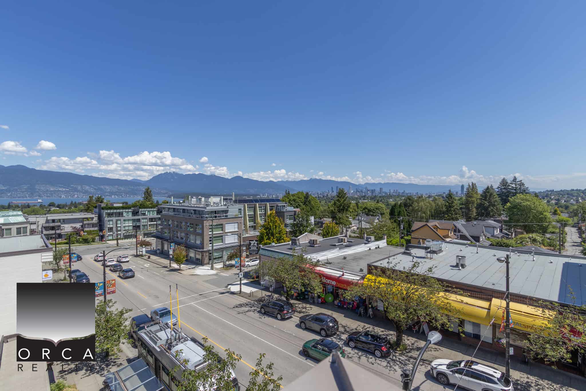 Vibrant cityscape view from a high-rise balcony showcasing commercial and residential buildings, green spaces, and distant mountains, ideal for Vancouver real estate and property investment in BC.