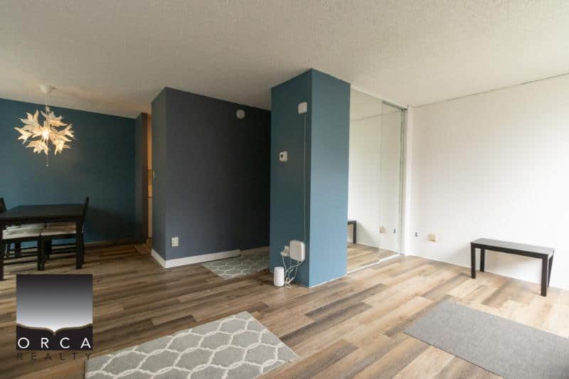 Spacious modern living room with hardwood floors, blue accent walls, and natural light, offered by Orca Realty Inc. in Vancouver’s real estate market.