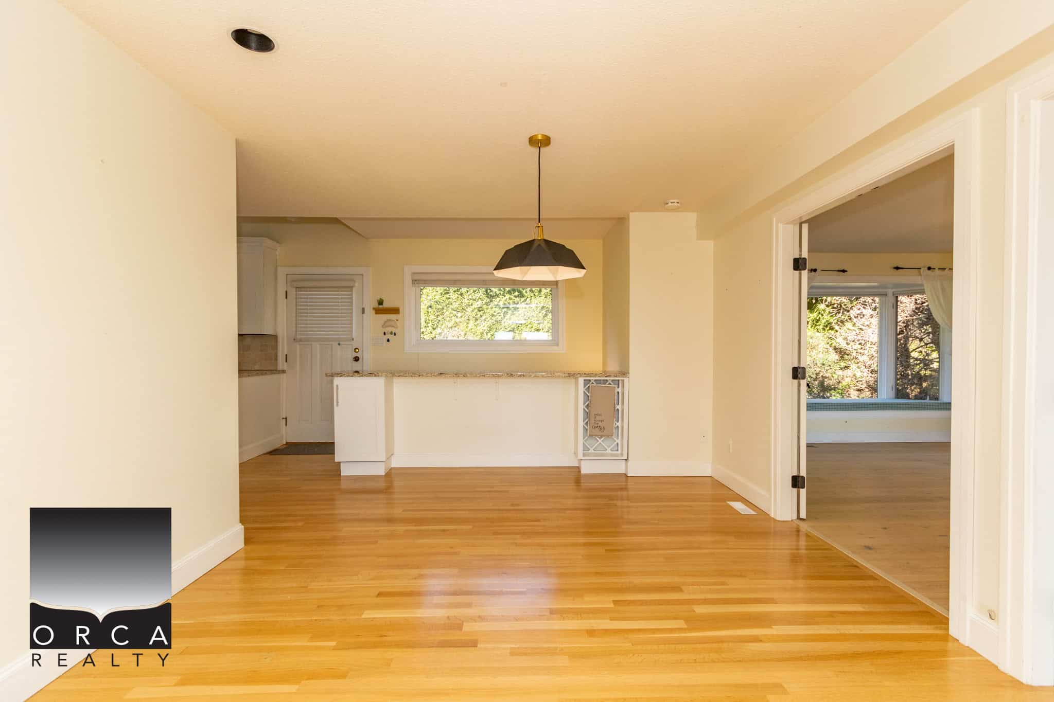 Bright open concept living area with hardwood floors and large windows, featuring a modern kitchen and cozy dining space in a Vancouver Island home listed by Orca Realty Inc.