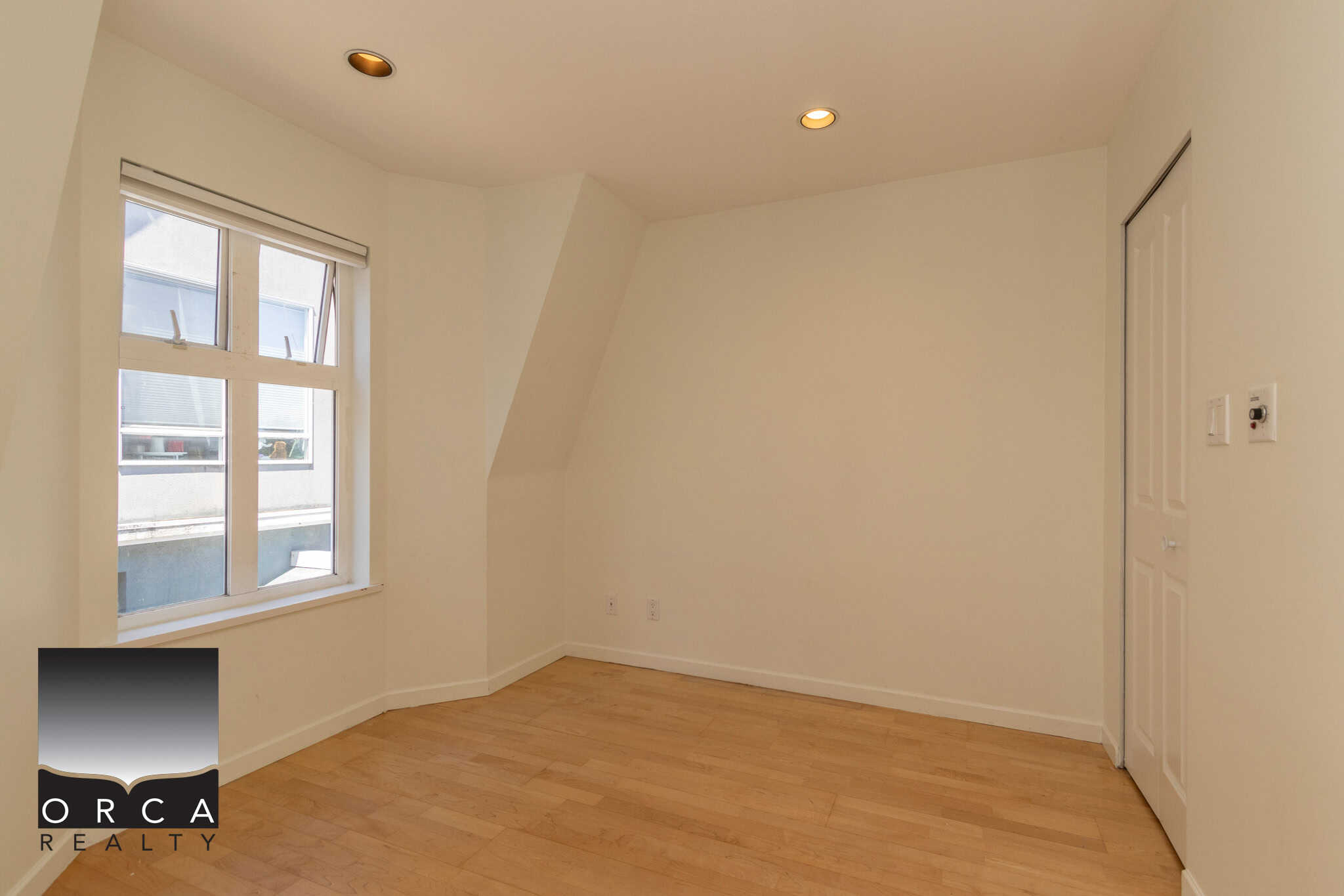 Bright empty bedroom with large window, white walls, hardwood flooring, and overhead lighting, ideal for Vancouver Island real estate buyers seeking modern home interiors.