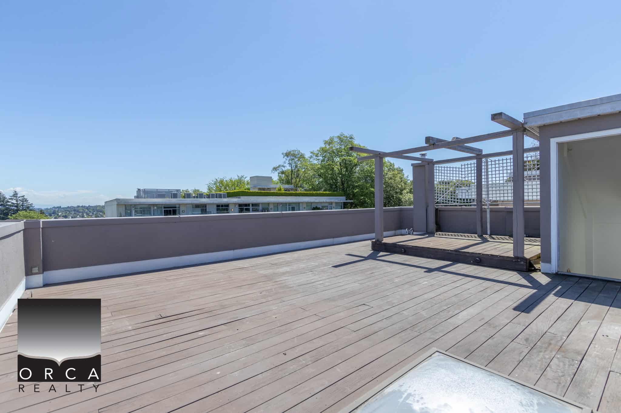 Spacious rooftop terrace with modern decking and a partial pergola, offering panoramic views and outdoor living space in a Vancouver-area property listed by Orca Realty Inc.