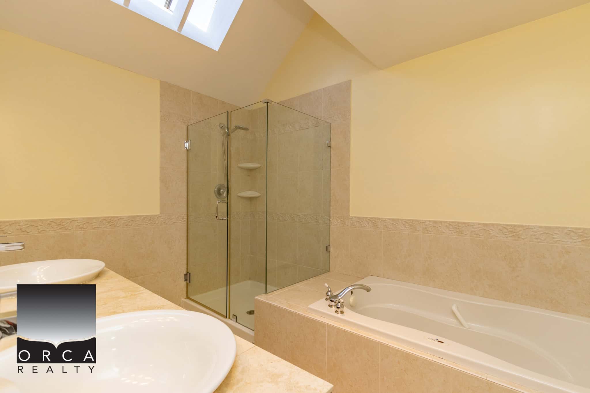 Bright modern bathroom with a glass shower, bathtub, dual sinks, and neutral tile finishes, perfect for comfortable living and property showcasing by Orca Realty Inc.