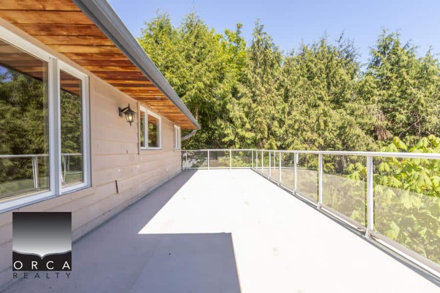 Spacious outdoor balcony with glass railing overlooking lush green trees, perfect for relaxing or entertaining in a serene outdoor setting.