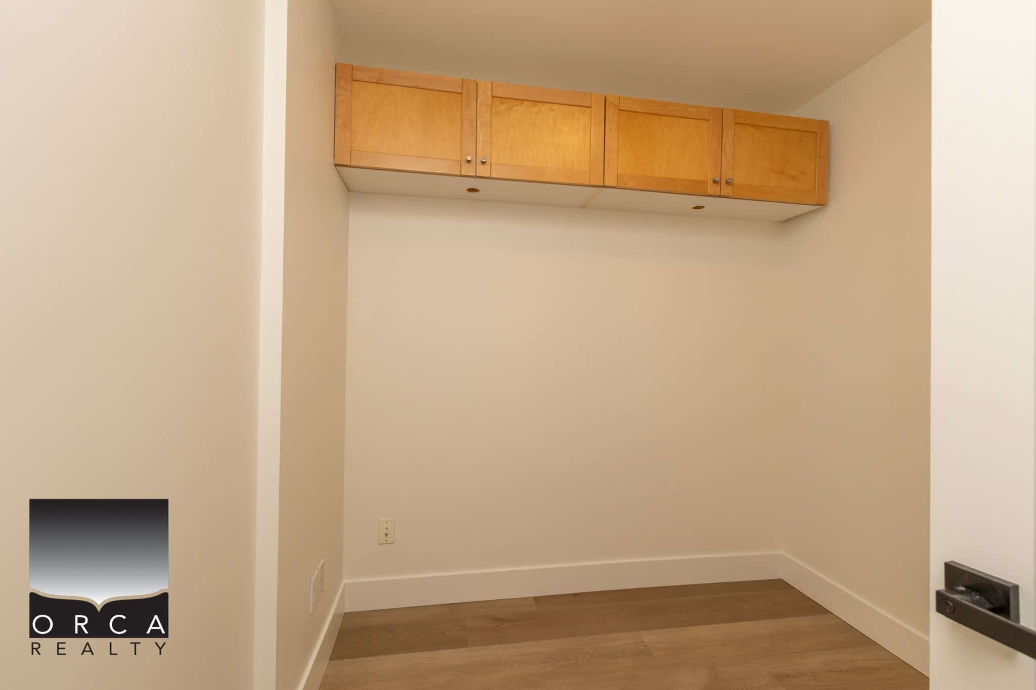 Spacious interior storage closet with wooden cabinets in a modern home. Perfect for organization in a residential property listed by Orca Realty Inc., offering optimal space for tenants or homeowners.