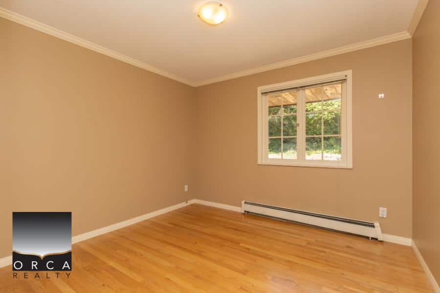 Bright empty living room with beige walls, hardwood flooring, and large window showing greenery outside, ideal for real estate listings.