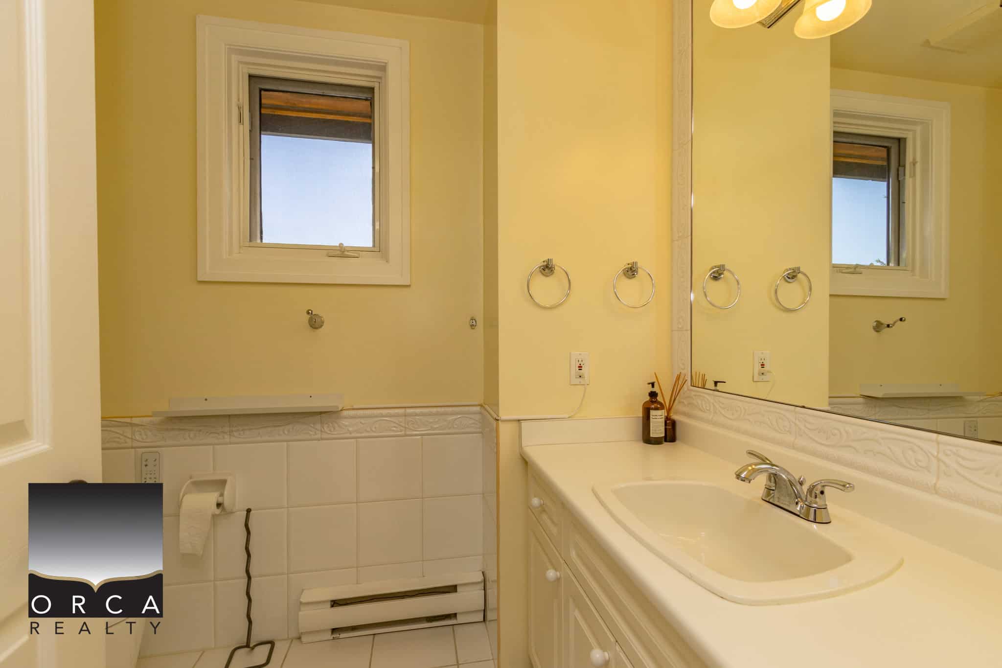 Bright yellow bathroom with white cabinetry and tile accents, featuring a single sink, mirror, and small windows for natural light, ideal for Vancouver Island home listings.