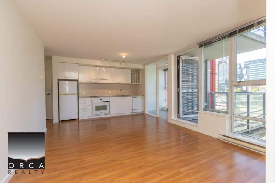 Modern Vancouver apartment with open-concept living room, hardwood floors, large windows, and updated kitchen, ideal for comfortable urban living and real estate investment in BC.