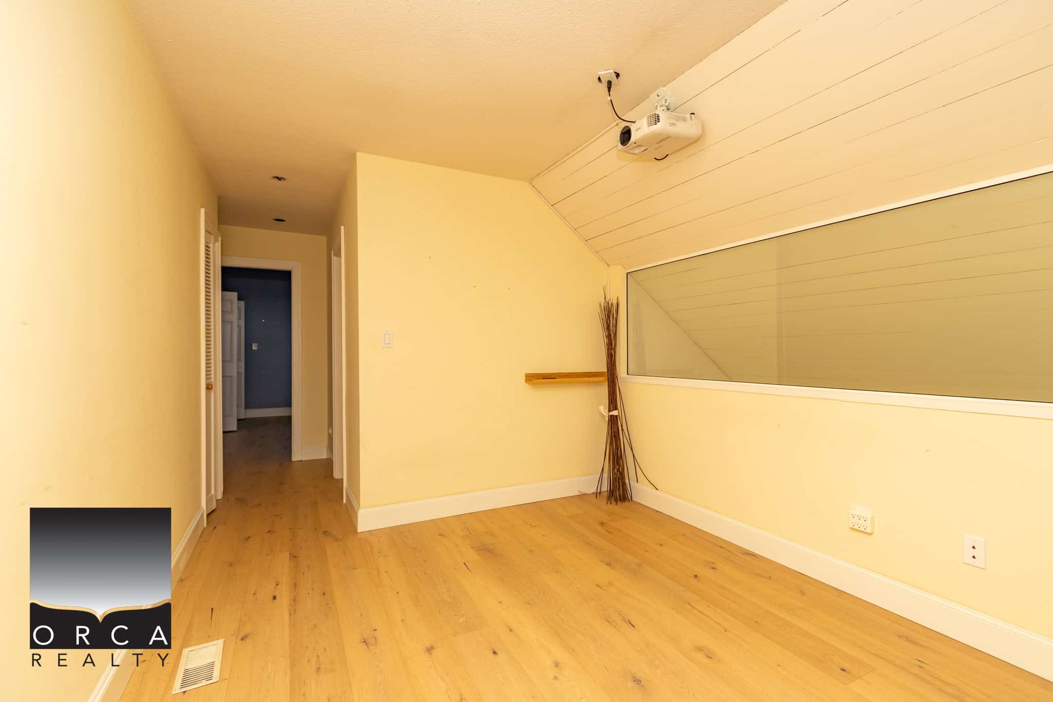Bright empty room with sloped ceiling, hardwood flooring, large glass window, and a ceiling-mounted projector, ideal for modern living or a home office in Vancouver.