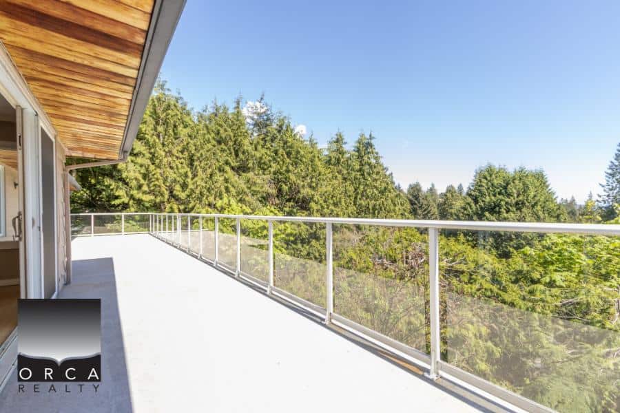 Balcony with glass railing overlooking lush green trees and blue sky, modern residential property, outdoor living space in Vancouver, BC.
