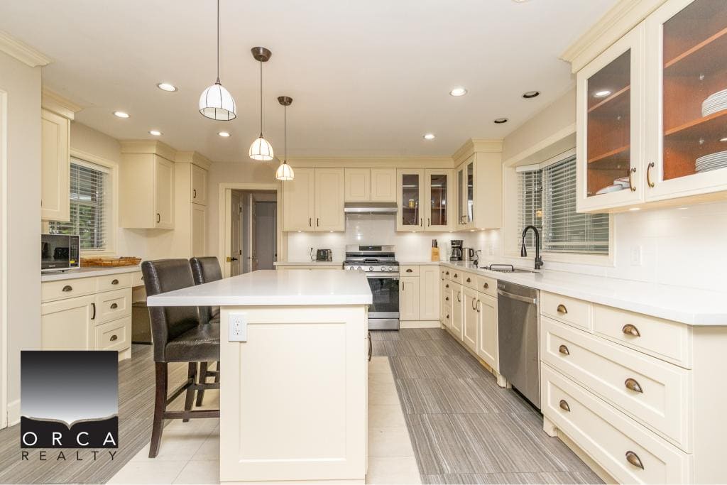 Bright modern kitchen with white cabinetry, stainless steel appliances, and a central island, perfect for family cooking and entertaining, offered by Orca Realty Inc. in British Columbia.