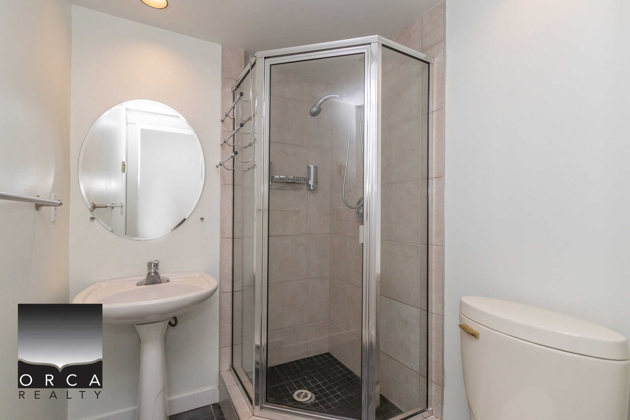 Modern bathroom vanity with round mirror, walk-in shower with glass enclosure, and a toilet in a well-maintained home, perfect for comfortable living.