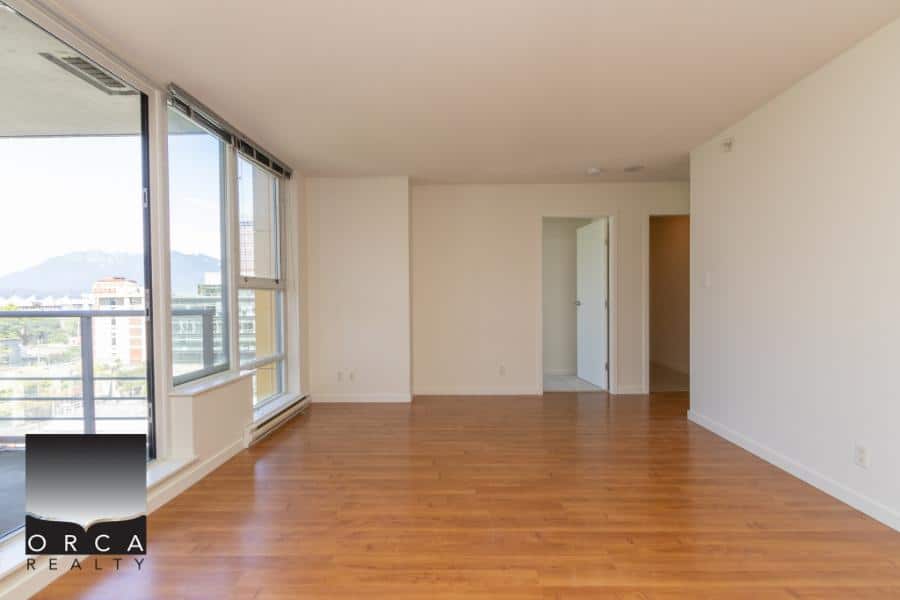 Spacious living room in modern apartment with large windows, hardwood flooring, and city view, available through Orca Realty Inc. for rent or sale in Vancouver, BC.