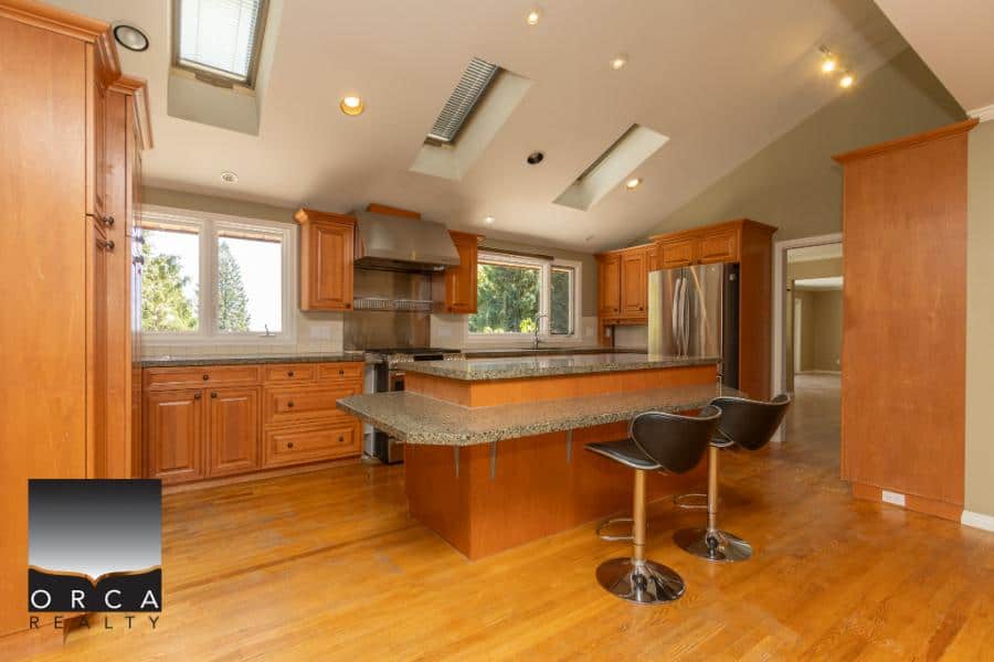 Spacious kitchen with wooden cabinetry, granite countertops, stainless steel appliances, and modern lighting, offering a perfect blend of style and functionality.