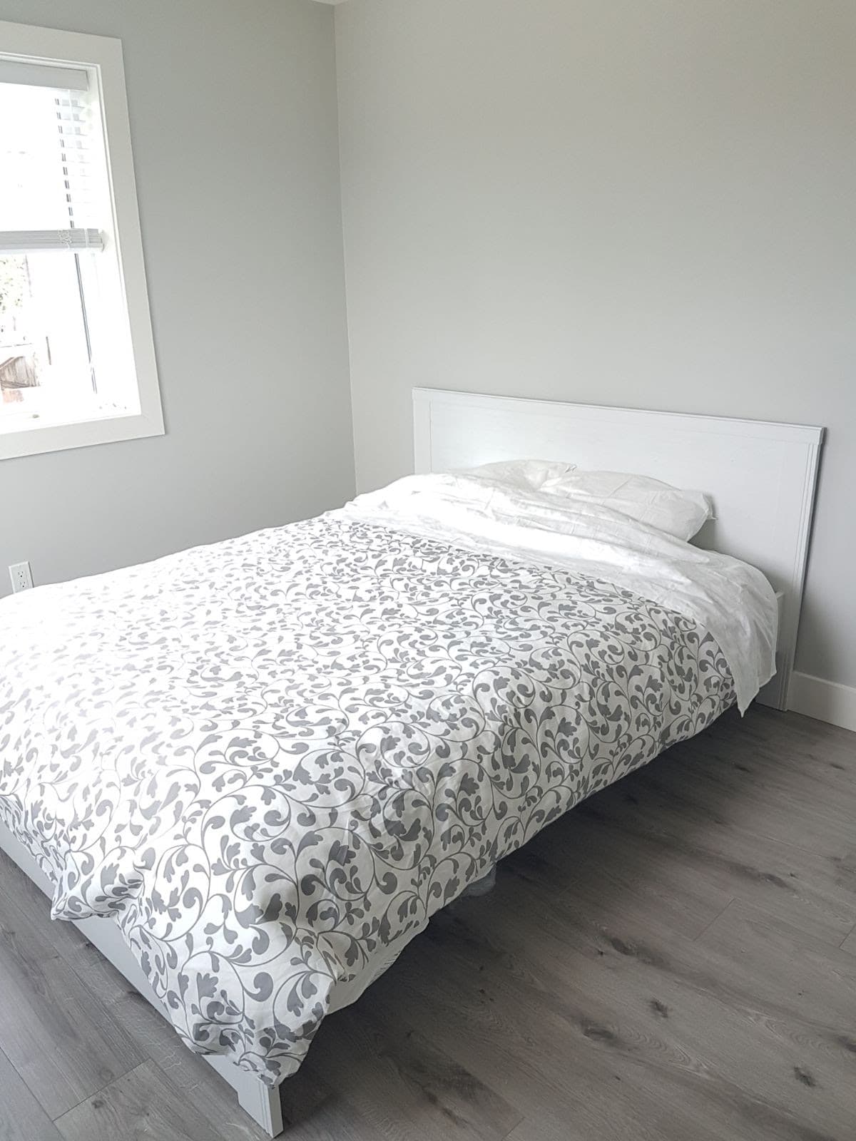 8 Modern bedroom with white bed frame and patterned bedding, natural light from window, minimalist decor, grey wood flooring.