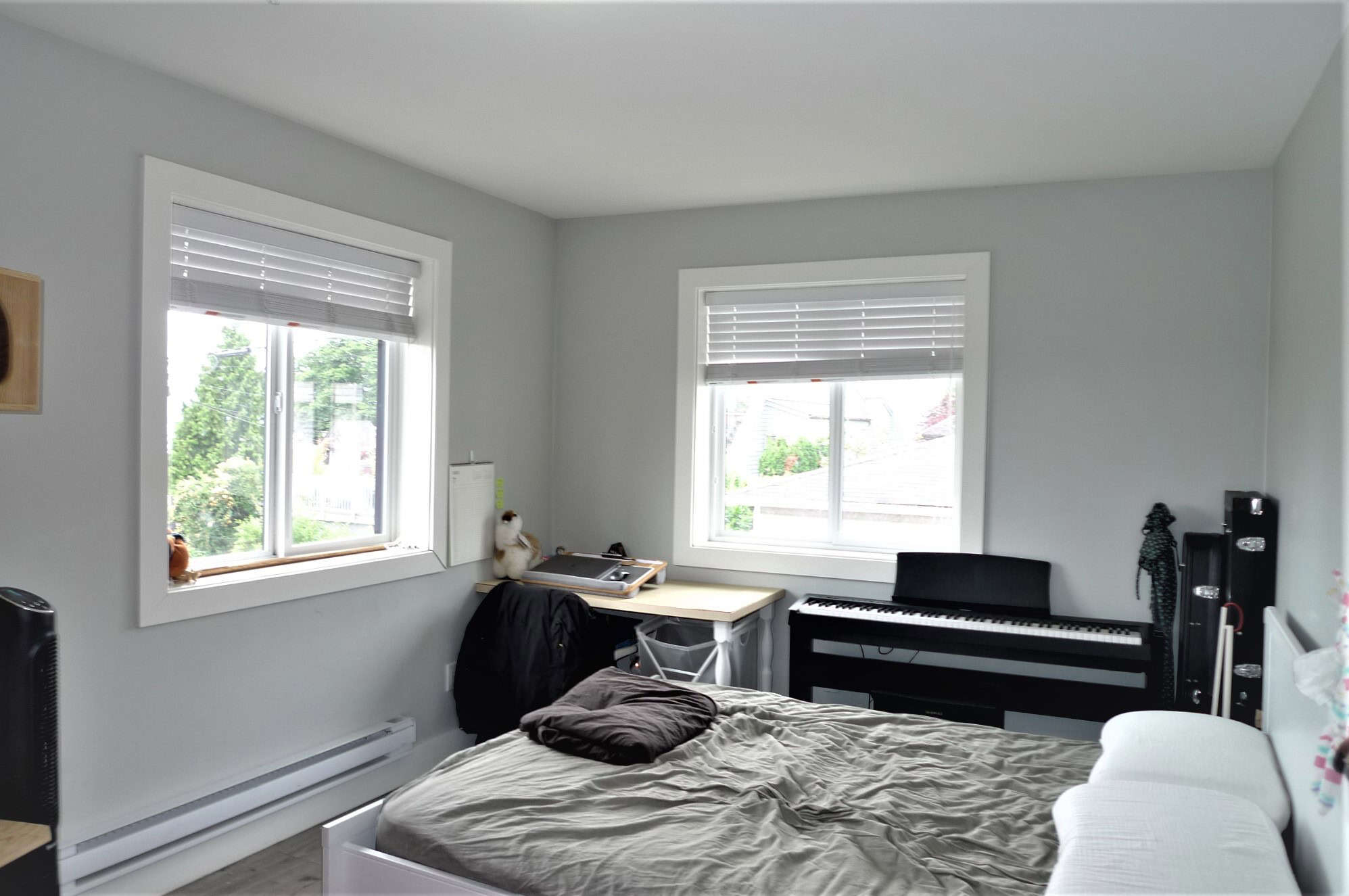 9 Bright bedroom with two large windows, grey walls, and modern decor, featuring a bed, digital piano, and workspace, ideal for Vancouver or Victoria homebuyers seeking stylish real estate.