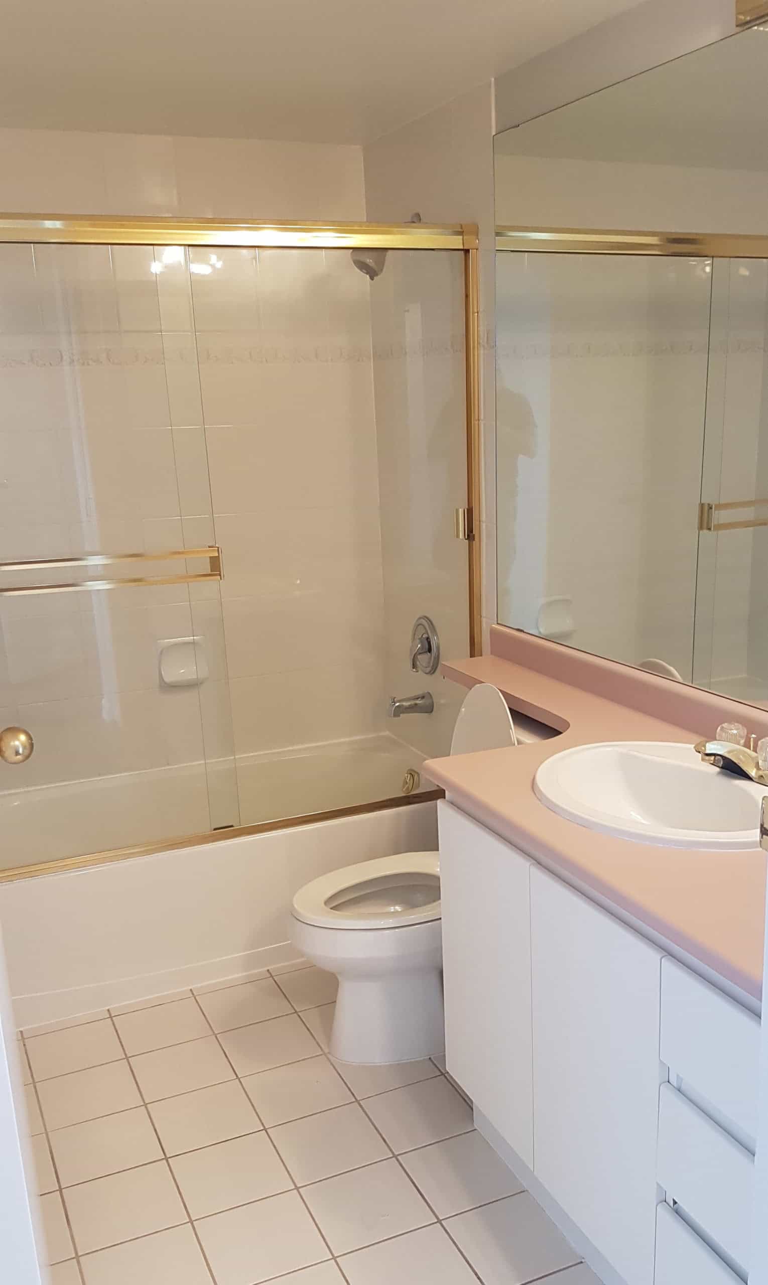 Clean bathroom with bathtub, shower, toilet, and pink sink vanity, featuring a large mirror and white tiled flooring, perfect for Vancouver area homebuyers seeking comfortable living spaces.