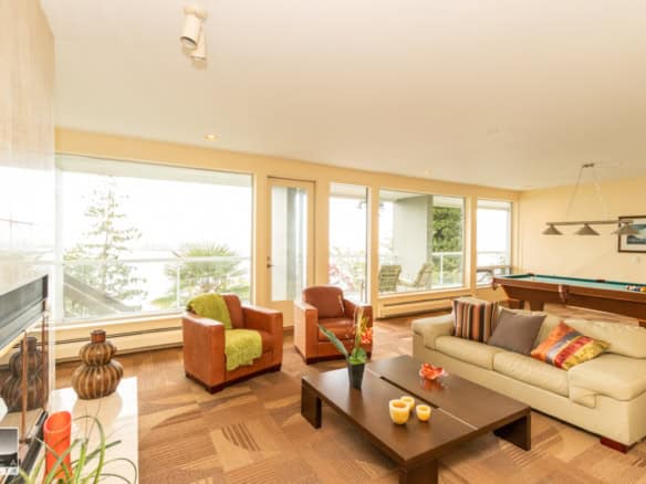 Bright ocean-view living room with large windows, contemporary furniture, and a pool table, perfect for relaxed family gatherings and entertaining guests.