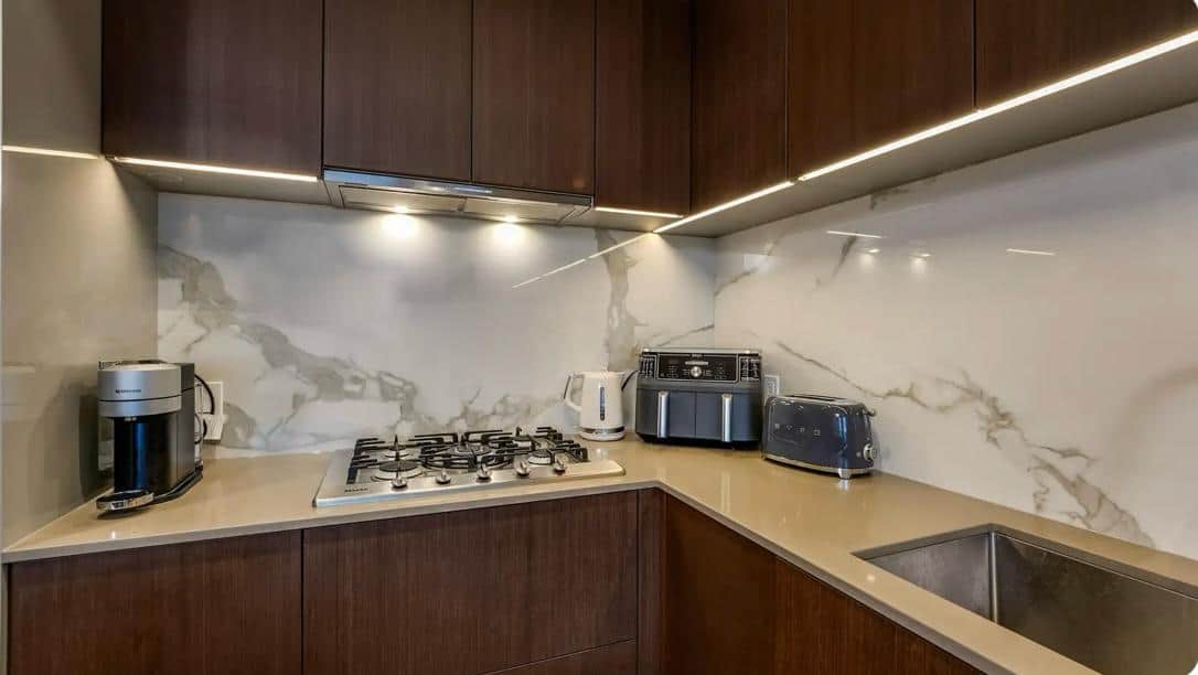 Modern kitchen with dark wood cabinetry, marble backsplash, and stainless steel appliances including a gas cooktop, toaster, kettle, and coffee maker, perfect for stylish urban living.