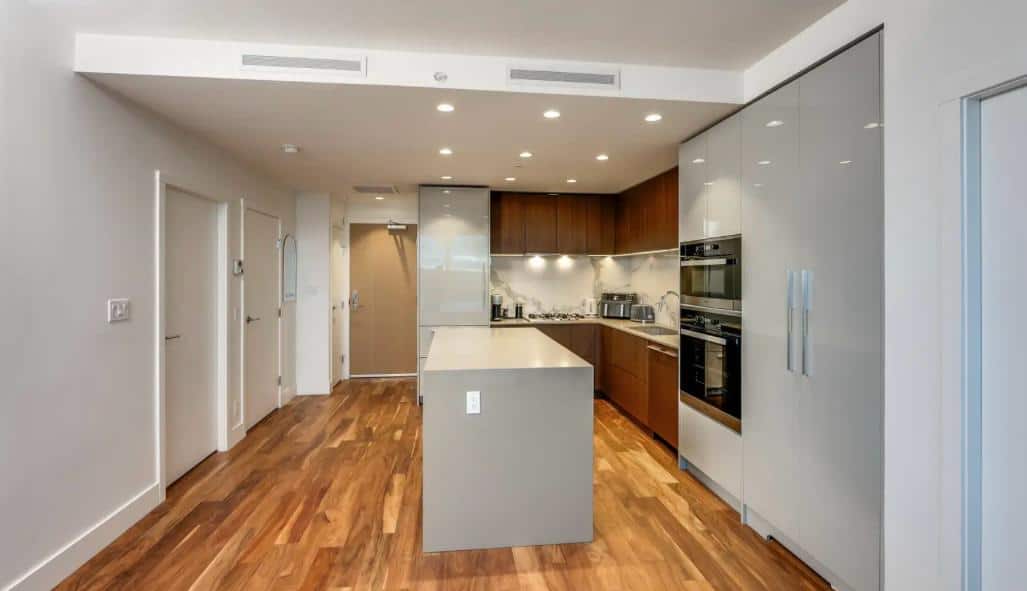 Modern kitchen with wooden flooring, sleek cabinetry, stainless steel appliances, and a central island in a contemporary condo or apartment, ideal for urban living.
