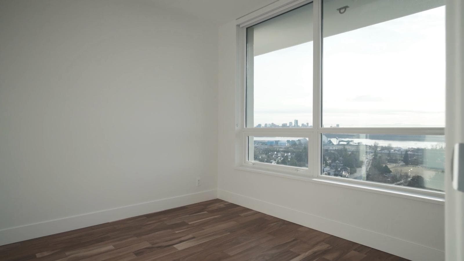 WhatsApp Image 2024-03-02 at 18.27.41 Bright vacant apartment room with large window view of city skyline and water, ideal for Toronto real estate buyers, with modern hardwood floors and minimalist decor.