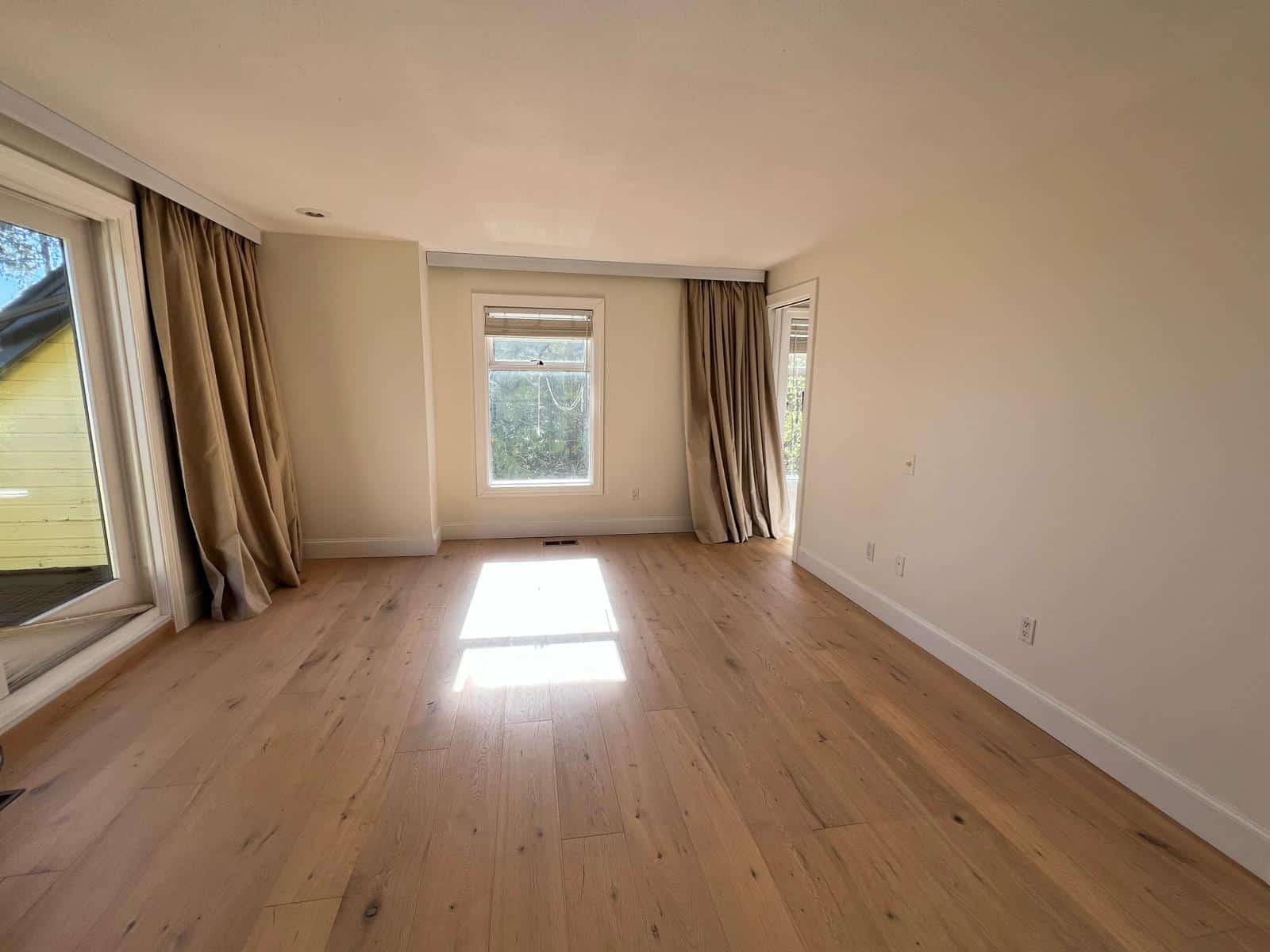 Bright and spacious living room with natural light, hardwood flooring, and large windows with beige curtains, perfect for Vancouver real estate and residential home sales.
