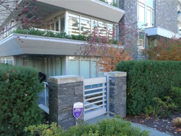 Modern multi-story residential building with secure gated entrance, surrounded by lush greenery and landscaped gardens, showcasing upscale Vancouver real estate options.