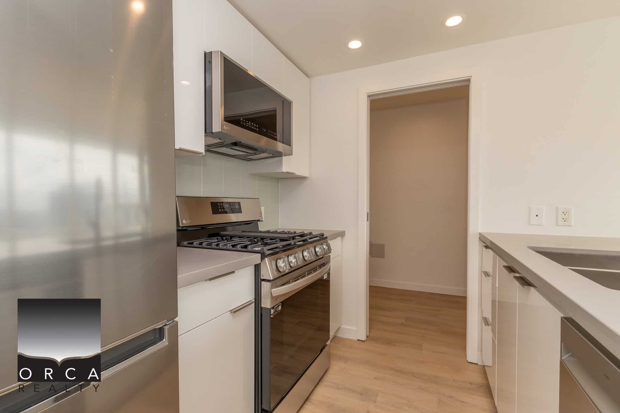 13 Spacious modern kitchen with stainless steel appliances, white cabinetry, and hardwood floors, ideal for Vancouver Island real estate buyers seeking contemporary condo features.