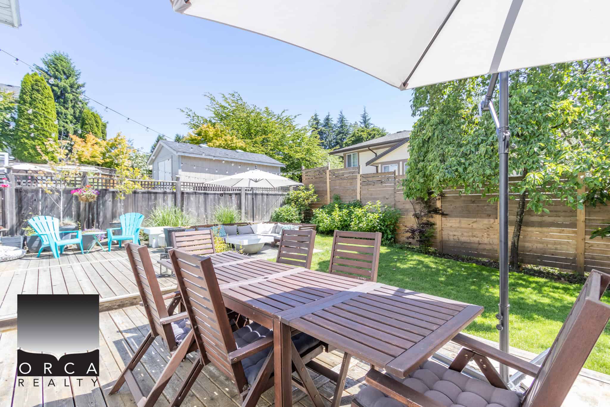 Spacious backyard patio with wooden dining set, colorful Adirondack chairs, and lush greenery, perfect for outdoor entertaining and relaxation in Vancouver, BC.