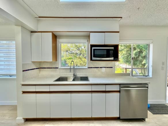 Bright modern kitchen with white cabinetry, stainless steel appliances, and ample natural light from large windows, ideal for Vancouver Island real estate listings.