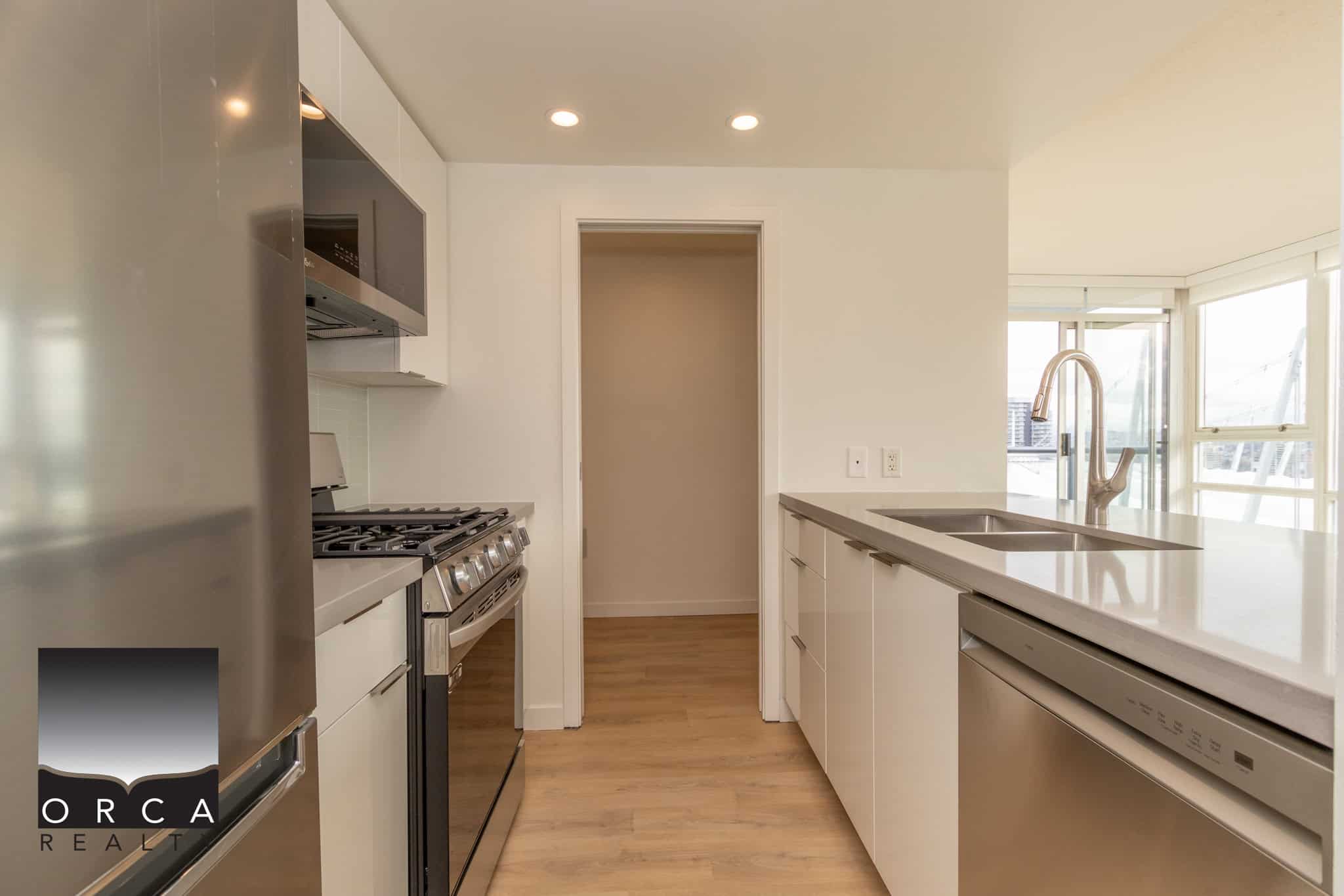 9 Contemporary stainless steel kitchen appliances in a modern condo, featuring a sleek design with white cabinetry, wood flooring, and large windows providing natural light and city views for urban living.