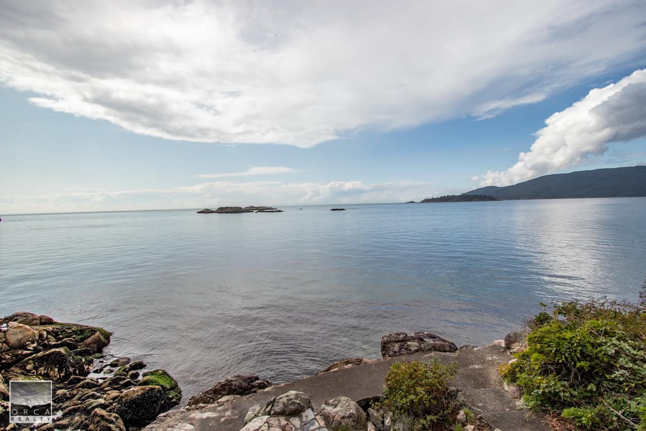 IMG_3073 Serene waterfront view of ocean with rocky shoreline, distant islands, and lush green hills, showcasing ideal real estate opportunities along British Columbia's coast, perfect for waterfront property investment.
